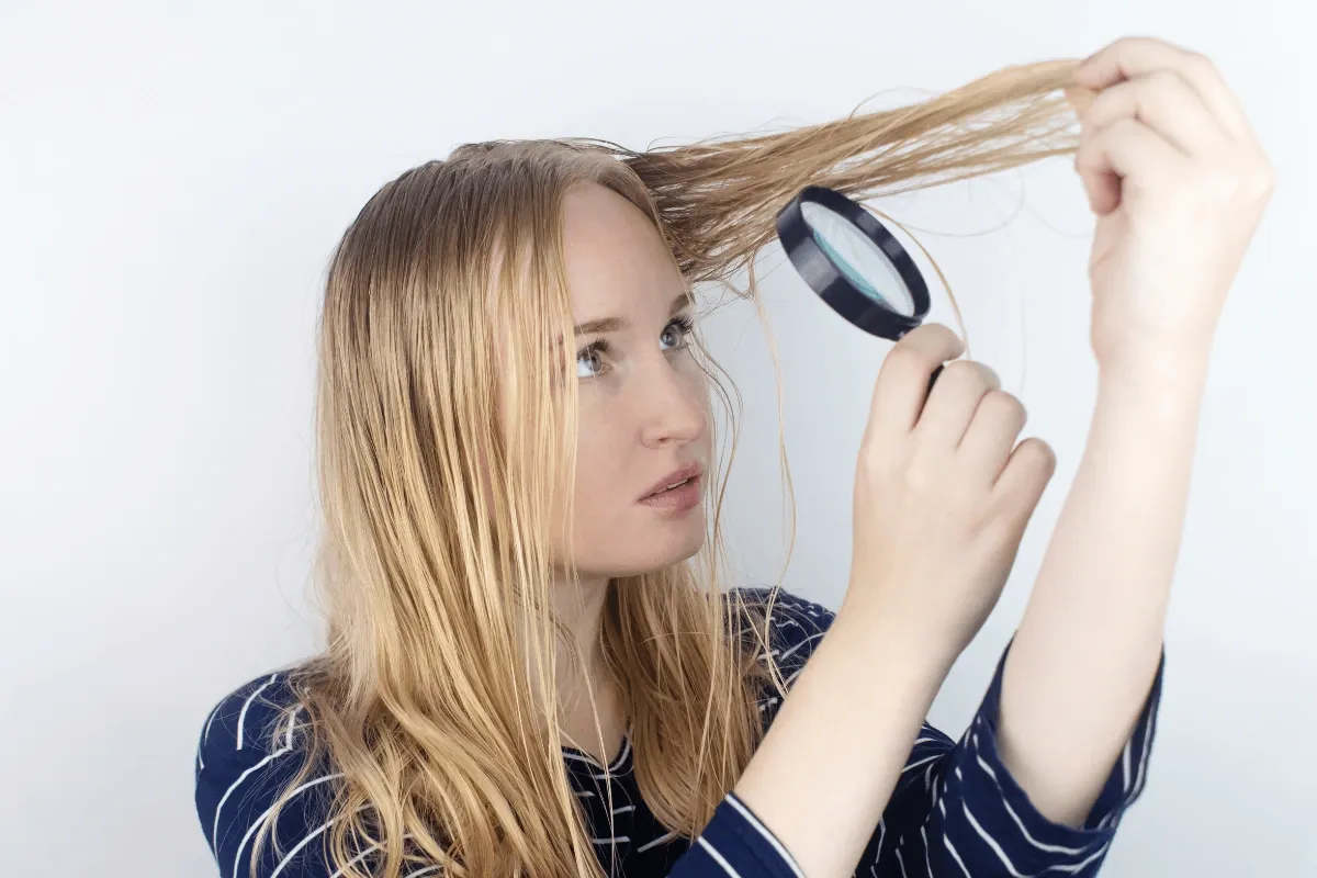 Dlouhé rovné medově blond vlasy, pohled do lupy držené u pramene, tmavé pruhované triko