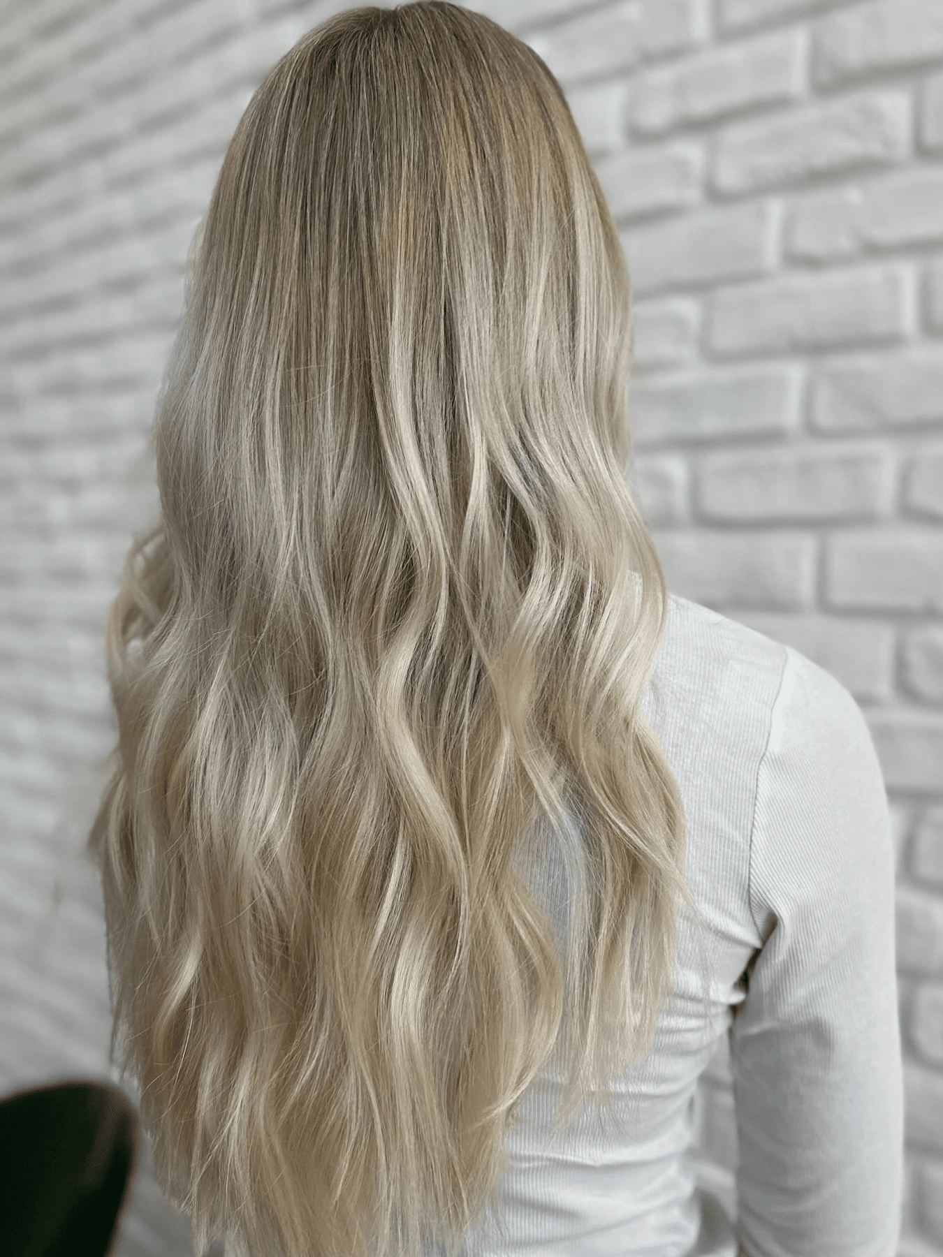 Airtouch se střihem: dlouhé blond vlasy s jemnými vlnami v délkách, bílá cihlová zeď (Klára Valnerová)