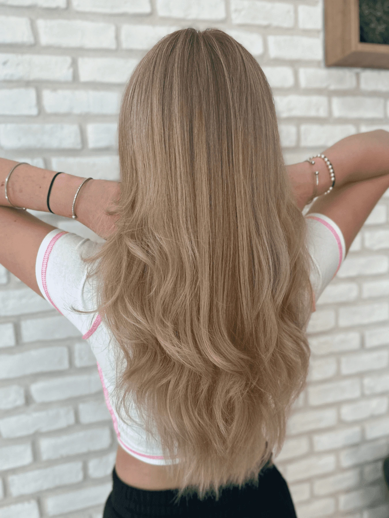 Butterfly cut: velmi dlouhé hladké vlasy v teplé písečné blond s jemnými vlnami na koncích, před cihlovou stěnou