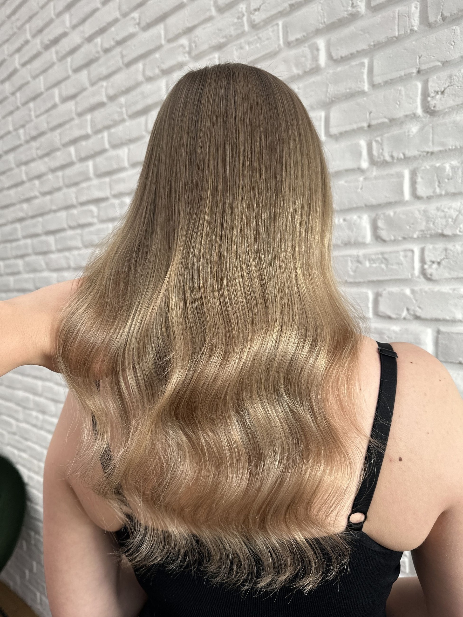 Kreativní barvení: dlouhé vlnité vlasy ve zlaté blond, ruka zleva drží prameny (Sára Hedbávná)
