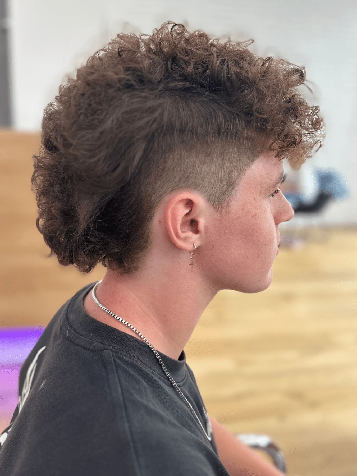 Mullet: hustě kudrnaté hnědé vlasy, objemný vršek, krátce vyholené boky