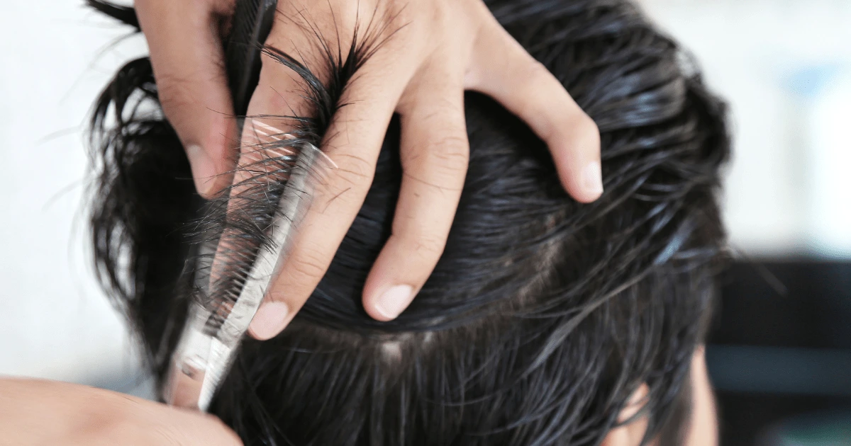Pixie cut: ruce zastřihují nůžkami tmavé vlhké vlasy u temene